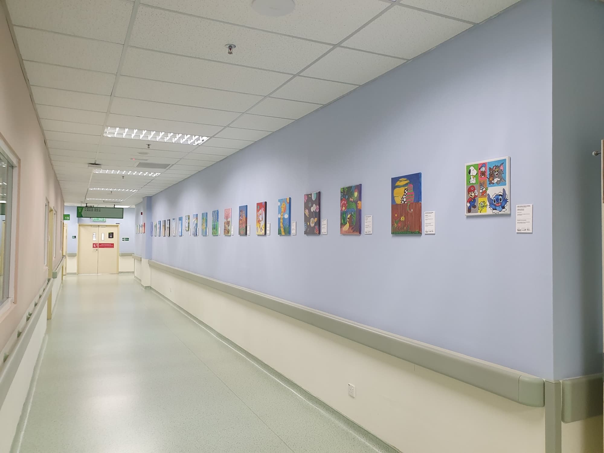 Children's paintings displayed along a hospital corridor wall